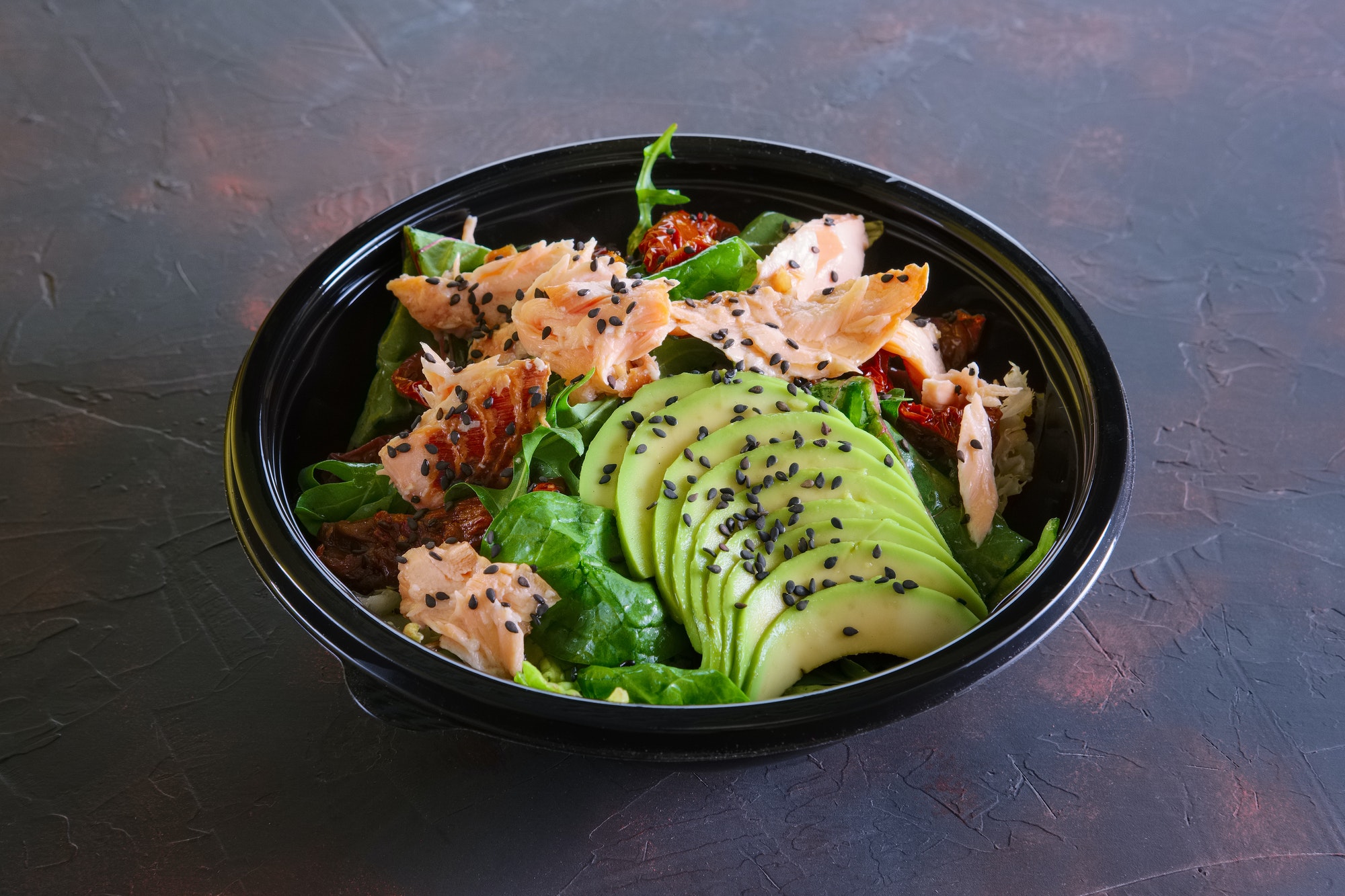 Salad with salmon, avocado and sun dried tomatoes in take away packaging